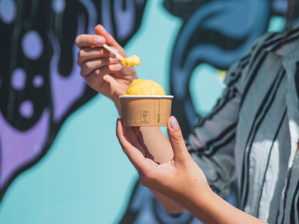 a paper gelato cup lined with a plant based bioplastic, a scoop of gelato, a wooden spoon to eat the gelato